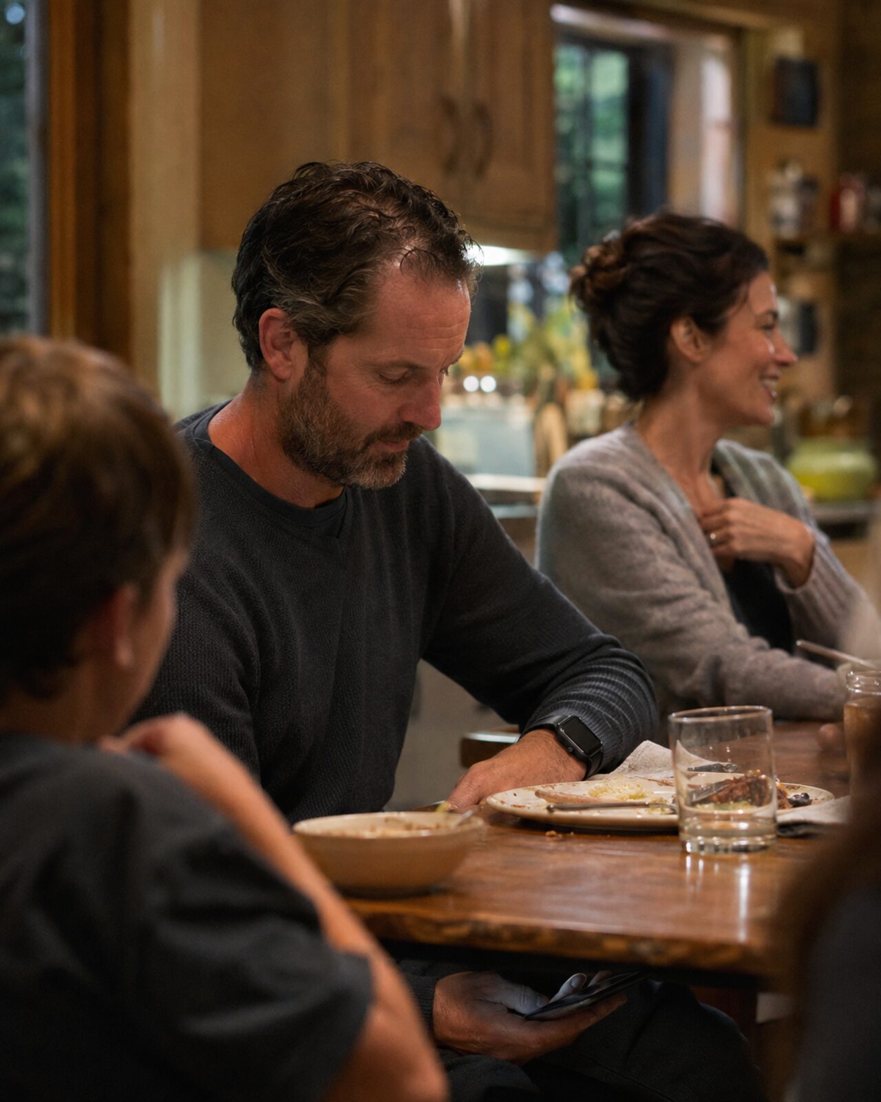 A man in his forties at a dinner table, glancing at the Simone app with relief