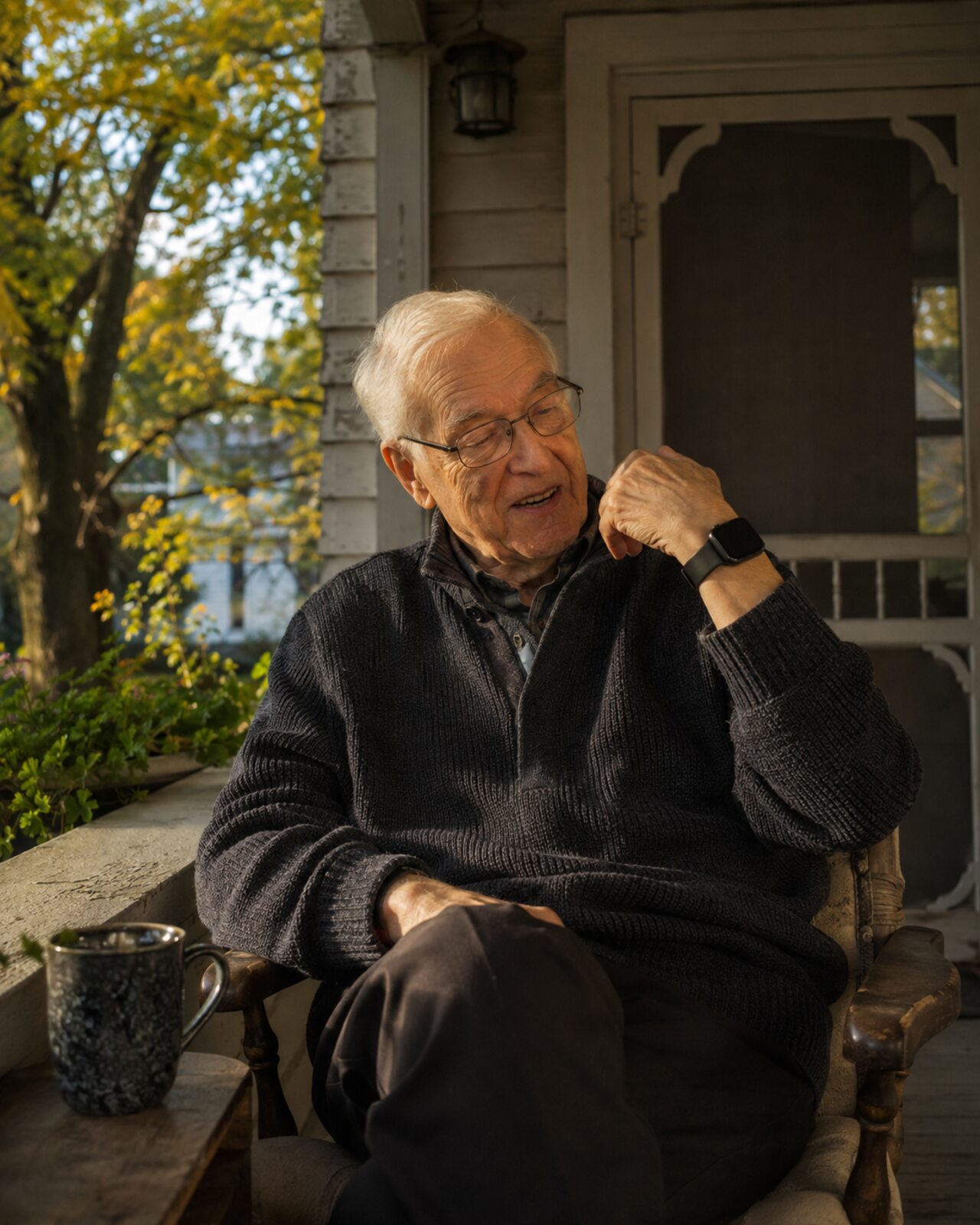 An older man on a porch in the evening, talking into the watch on his wrist and smiling